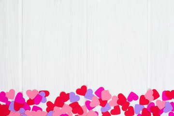 Bottom border of colorful Valentines Day paper hearts against a white wood background