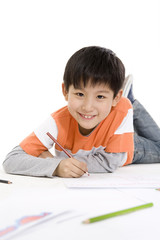 A young boy coloring while lying on the floor