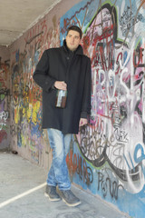 Young man holding bottle of brandy leaned on graffiti wall