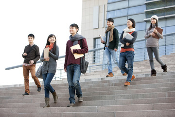 Obraz premium Young college students walking down steps of university building
