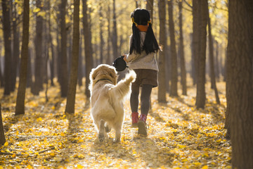Little girl running with dog in autumn woods