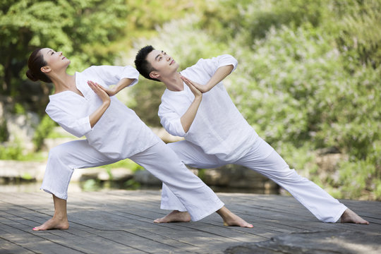 Man and woman practicing yoga on a wooden dock