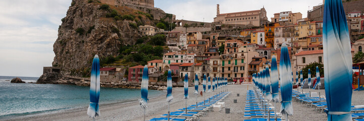 Blue umbrella and beachchair at  the beach in front of small italian town on cliff under blue sky
