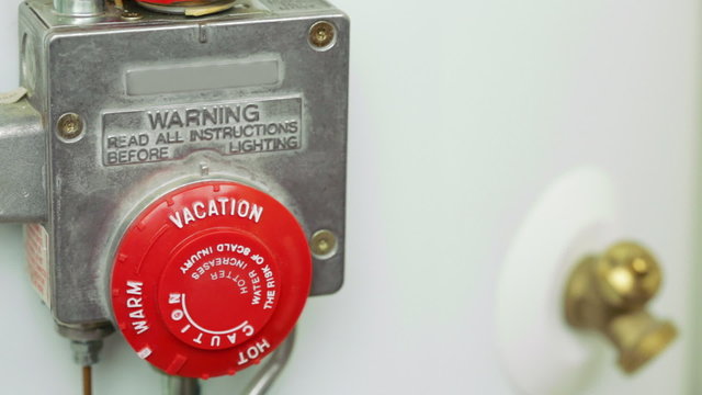 Hand turning the temperature dial of a water heater to the VACATION setting.
