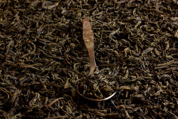 Black tea in a metal spoon on a black tea background