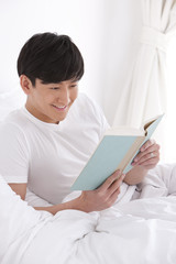 Young man reading a book in bed