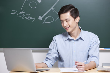 Cheerful male teacher using laptop in classroom