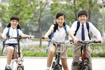 Obraz premium Happy schoolchildren in uniform with bicycles outdoors