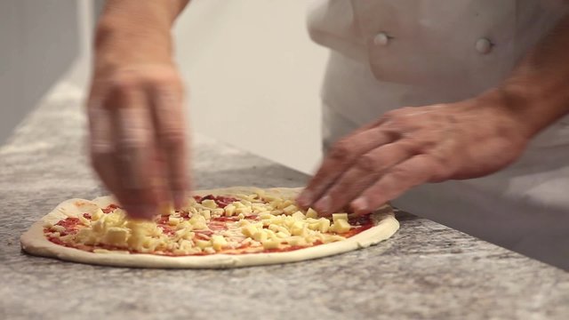 Unrecognizable man putting cheese topping on his pizza base 