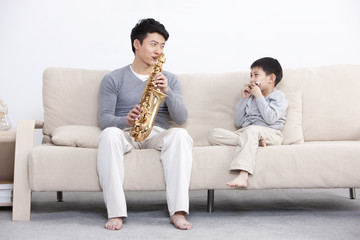 Joyful father and son playing saxophone and harmonica at home