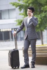 Young businessman talking on the phone with suitcase
