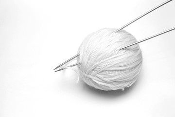 ball of white wool yarn with knitting needles on white backgroun