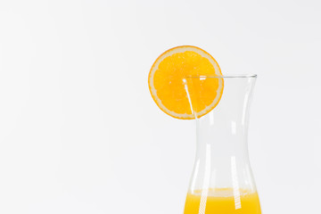 Glaskaraffe gefüllt mit Orangensaft. Eine Orangenscheibe steckt auf dem Rand.