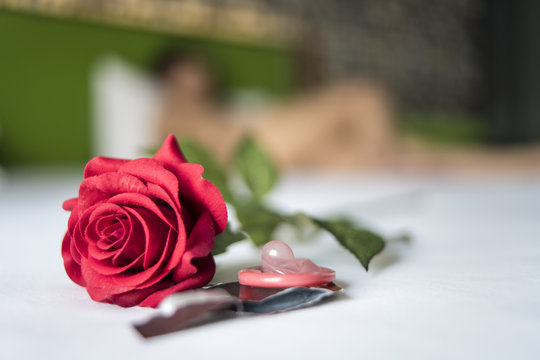 Condom and red rose on bed with woman on background