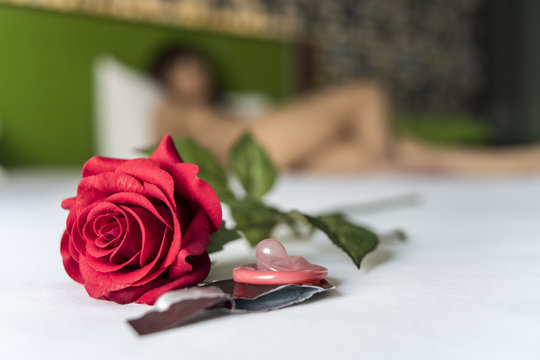 Condom and red rose on bed with woman on background