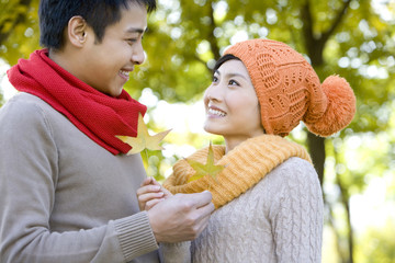 Young Couple in a Park in Autumn Holding Golden Maple Leaves - obrazy, fototapety, plakaty