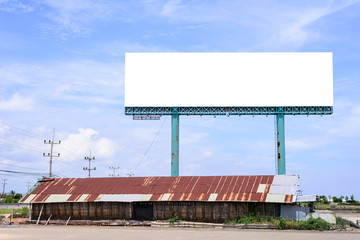 Blank billboard behind rusty roof of salt shed with blue sky for