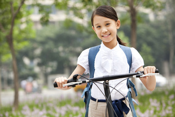 Happy schoolgirl in uniform with bicycle outdoors