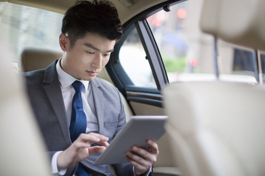 Businessman using digital tablet while traveling by car