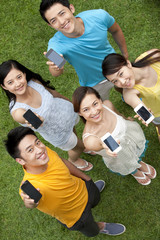 young people showing mobile phones on meadow