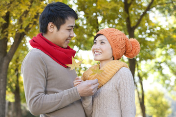 Young Couple in a Park in Autumn Holding Golden Maple Leaves