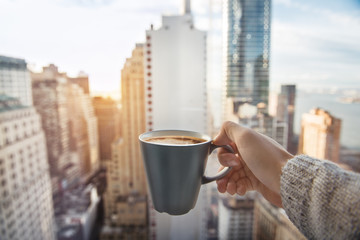 Man holding coffee cup in luxury penthouse apartments with view to New York City Manhattan downtown...