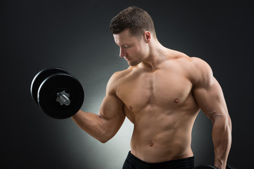 Fototapeta na wymiar Determined Muscular Man Exercising With Dumbbells