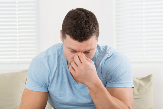 Man With Headache Pinching His Nose At Home