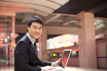 Portrait of smiling businessman using a laptop at station