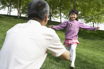 Naklejka premium Young Girl Running Towards Man In Park With Arms Outstretched