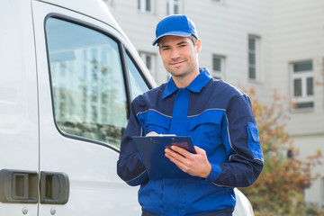 Delivery Man In Uniform Holding Clipboard By Truck