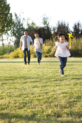 Young Chinese girl playing in a field with a pinwheel with her family