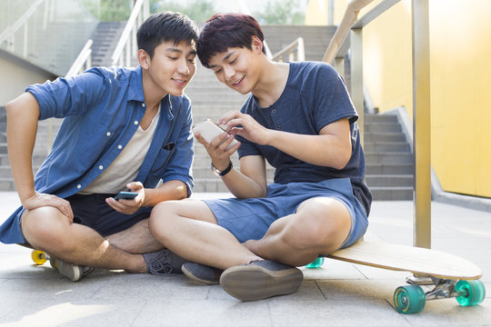 Young men using smartphone while sitting outdoors
