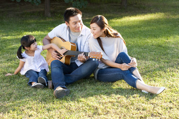 Young Chinese family in a park with a guitar