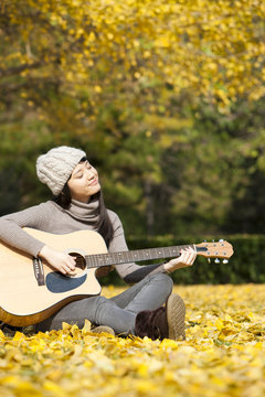 Lovely female college student with guitar bathed in the autumn sun's rays on campus