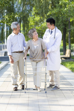 Senior woman walking with walking frame under doctor and  husband's assistance