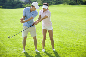 Young man teaching his girlfriend how to play golf