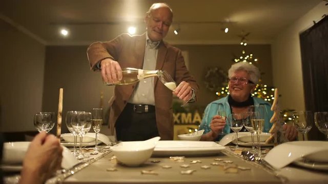 4k footage, happy seniors on dining table at home on christmas evening, one pouring champagne in glasses, captured with atomos shogun
