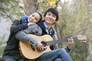 A young man plays the guitar as he girlfriend leans on him affectionately