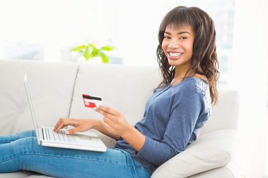Casual smiling woman using laptop while holding a card