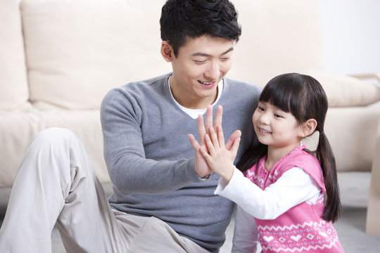 Happy father and little daughter doing high-five at home