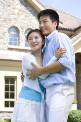 Smiling young couple in front of house