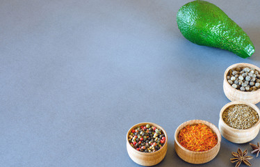 Avocado and spices in wooden bowls on a gray background
