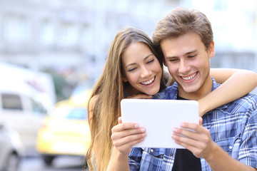 Happy couple sharing a tablet in the street