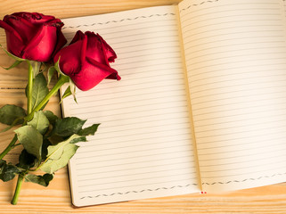 rose and empty notebook page on wood background