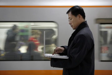 A Man Uses His Laptop As The Subway Train Passes By In The Background