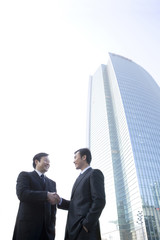 Businessmen shaking hands in front of tall building