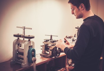 Goldsmith crafting precious metal with the help of rolling mill.