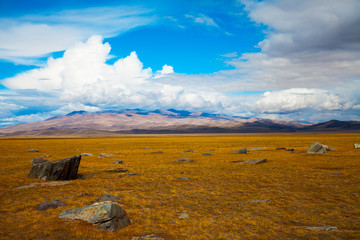 Multicolored steppe landscape with large stone in the foreground, mountains view, blue sky with clouds. Chuya Steppe, Kuray steppe in the Siberian Altai Mountains, Russia