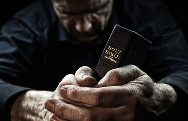 Obraz premium Modlący się mężczyzna trzyma Świętą Biblię.